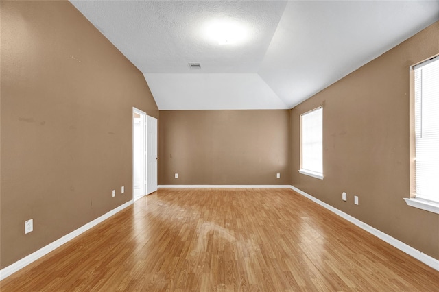 unfurnished room with visible vents, a textured ceiling, light wood-style floors, baseboards, and vaulted ceiling