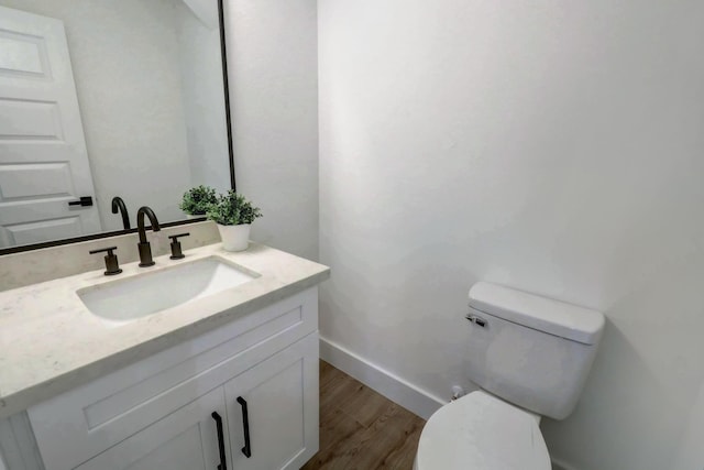 bathroom with vanity, toilet, wood finished floors, and baseboards