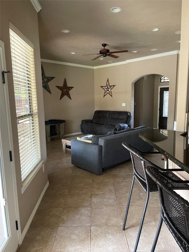 living area with a ceiling fan, arched walkways, a wealth of natural light, and ornamental molding