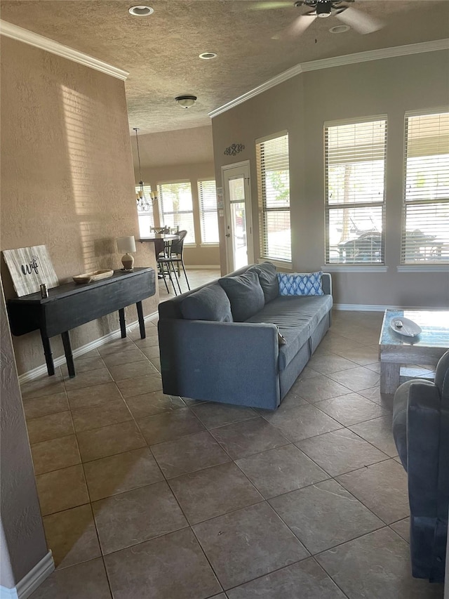 living room featuring baseboards, dark tile patterned flooring, ornamental molding, a textured ceiling, and ceiling fan with notable chandelier