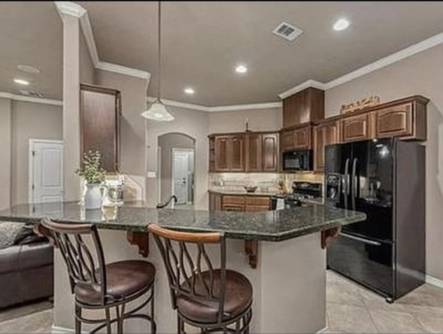 kitchen featuring visible vents, a peninsula, arched walkways, black appliances, and a kitchen breakfast bar