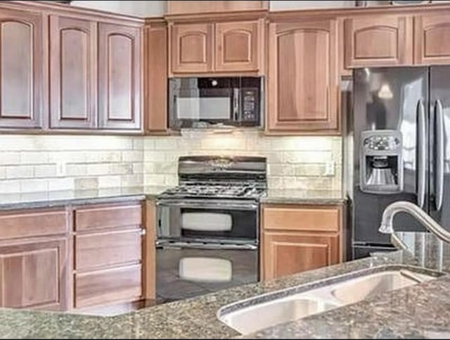 kitchen with backsplash, dark stone countertops, black appliances, and a sink