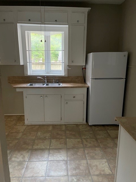 kitchen with white cabinets, light countertops, freestanding refrigerator, and a sink