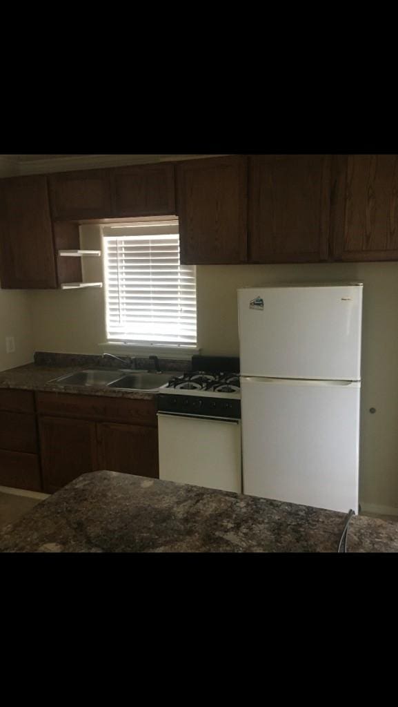 kitchen featuring open shelves, dark stone counters, freestanding refrigerator, and a sink