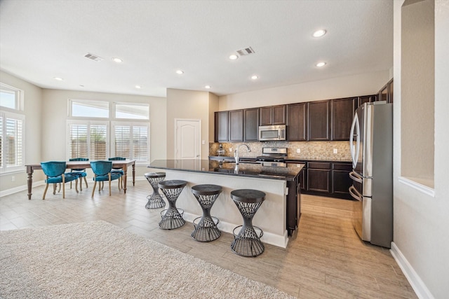 kitchen with visible vents, backsplash, dark brown cabinetry, a breakfast bar area, and stainless steel appliances