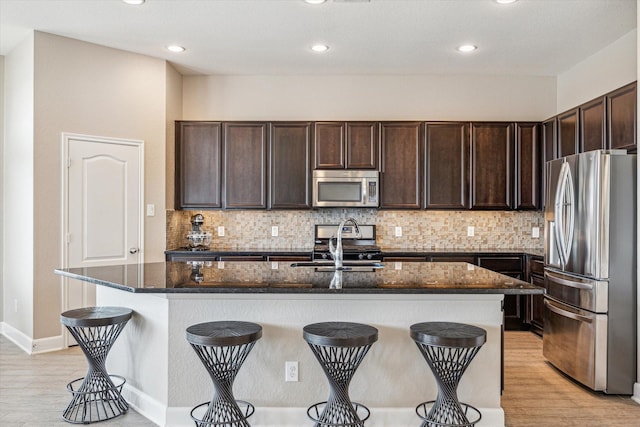 kitchen featuring dark stone countertops, stainless steel appliances, dark brown cabinetry, and a breakfast bar