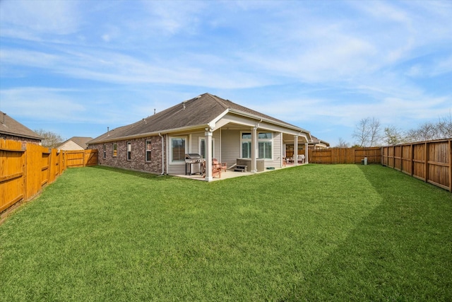 back of property featuring a yard, a fenced backyard, brick siding, and a patio