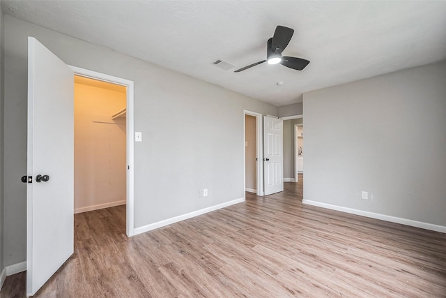 unfurnished bedroom with visible vents, a walk in closet, ceiling fan, baseboards, and wood finished floors