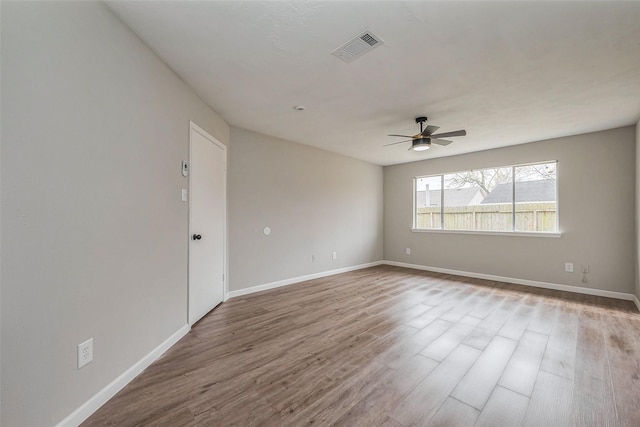 spare room featuring wood finished floors, a ceiling fan, visible vents, and baseboards