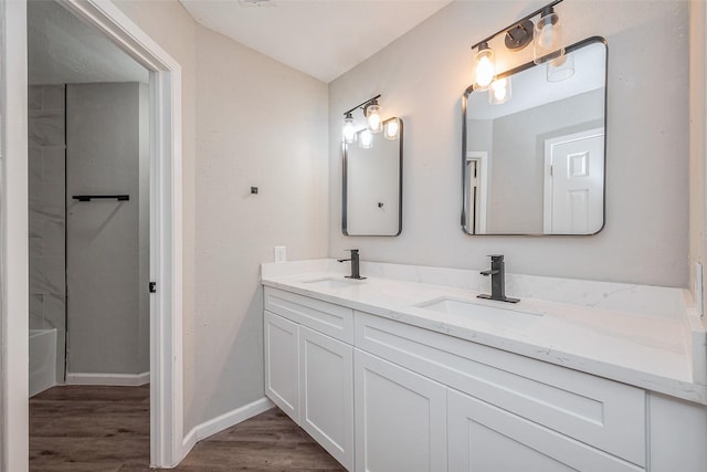 bathroom with double vanity, wood finished floors, baseboards, and a sink