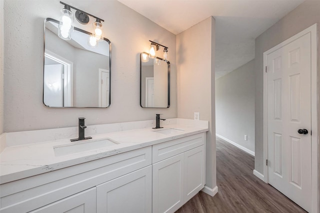 bathroom featuring double vanity, wood finished floors, baseboards, and a sink