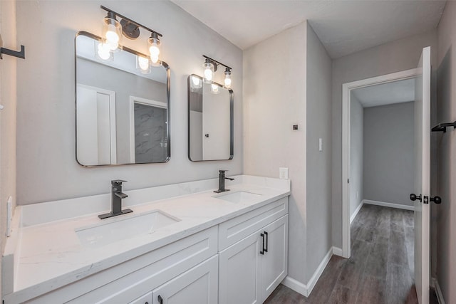 full bath with double vanity, wood finished floors, baseboards, and a sink