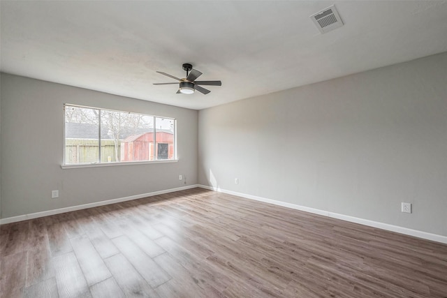 spare room featuring baseboards, wood finished floors, visible vents, and ceiling fan