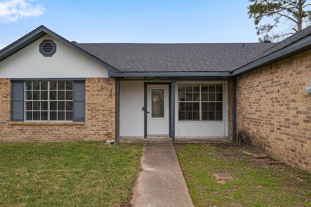 doorway to property featuring brick siding, a lawn, and a shingled roof