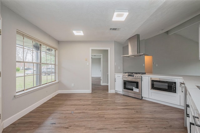 kitchen with visible vents, black microwave, gas range, wall chimney exhaust hood, and light wood-type flooring