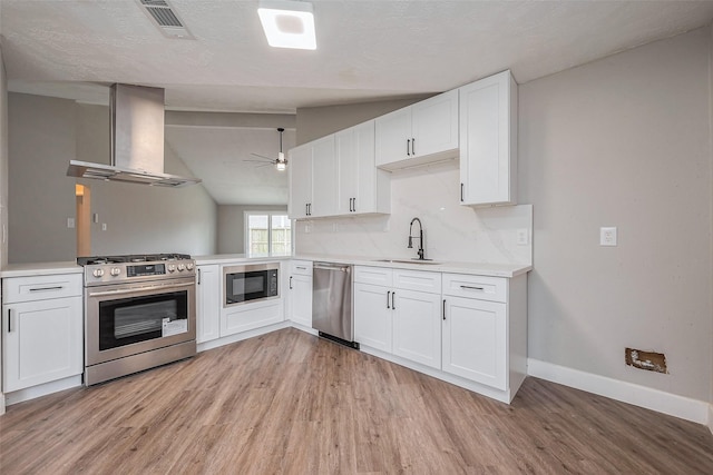 kitchen featuring light wood-type flooring, a sink, wall chimney range hood, stainless steel appliances, and light countertops