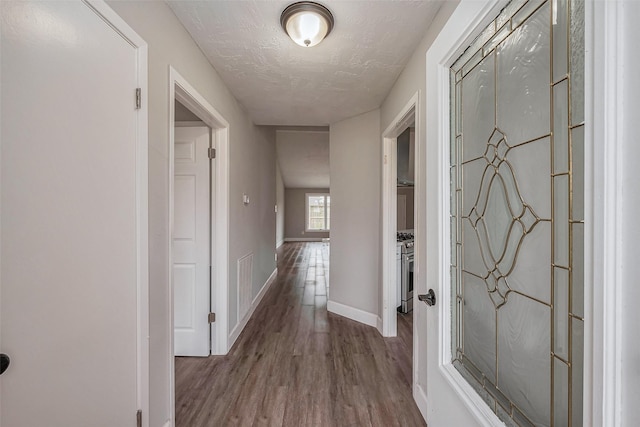 hallway featuring visible vents, a textured ceiling, baseboards, and wood finished floors