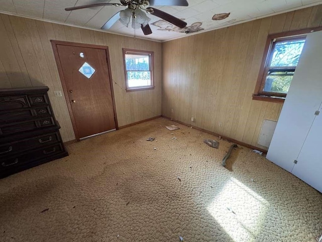 entrance foyer featuring wood walls, crown molding, ceiling fan, and carpet floors