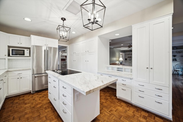 kitchen featuring white microwave, visible vents, a kitchen island, freestanding refrigerator, and black electric stovetop