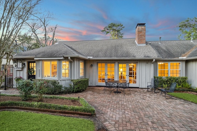 back of property with french doors, roof with shingles, board and batten siding, a chimney, and a patio area