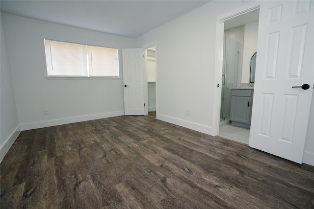 unfurnished bedroom with a walk in closet, ensuite bath, wood finished floors, and baseboards