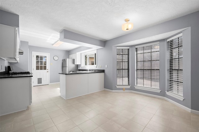 kitchen featuring dark countertops, white cabinetry, freestanding refrigerator, a peninsula, and range