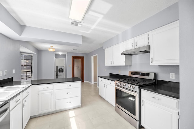 kitchen with dark countertops, under cabinet range hood, appliances with stainless steel finishes, a peninsula, and white cabinets