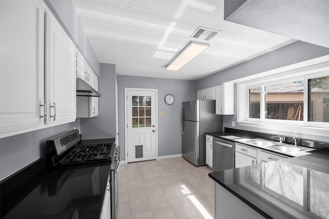 kitchen with dark countertops, visible vents, under cabinet range hood, white cabinets, and stainless steel appliances