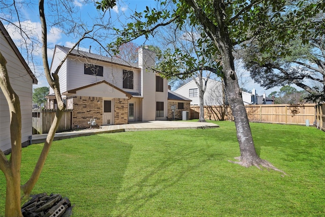 back of house with a patio, a fenced backyard, a chimney, a lawn, and brick siding