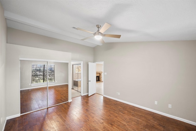 unfurnished bedroom featuring hardwood / wood-style flooring, a brick fireplace, baseboards, and lofted ceiling