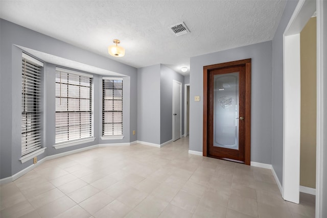 spare room with visible vents, baseboards, and a textured ceiling