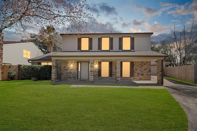 traditional home featuring brick siding, a porch, a front lawn, and fence