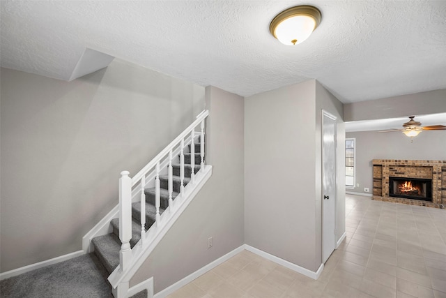 stairs with baseboards, a textured ceiling, ceiling fan, and a fireplace