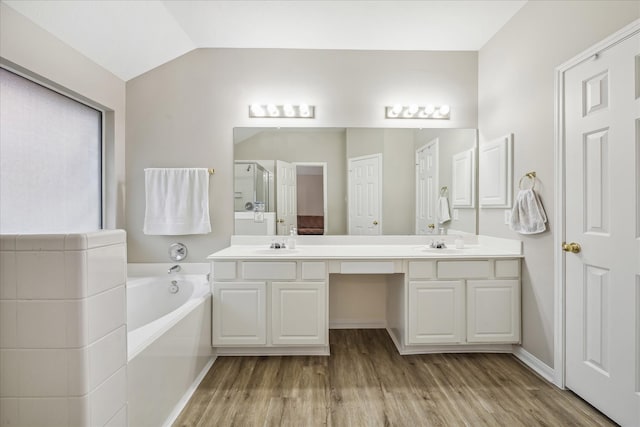 bathroom with a garden tub, a stall shower, wood finished floors, double vanity, and lofted ceiling