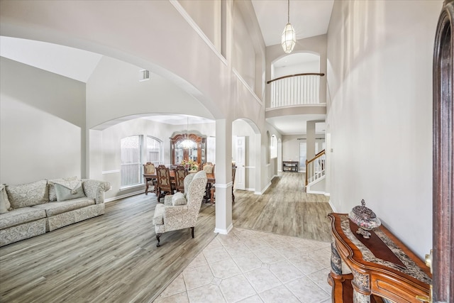 entryway with arched walkways, a notable chandelier, light wood-style flooring, and stairs