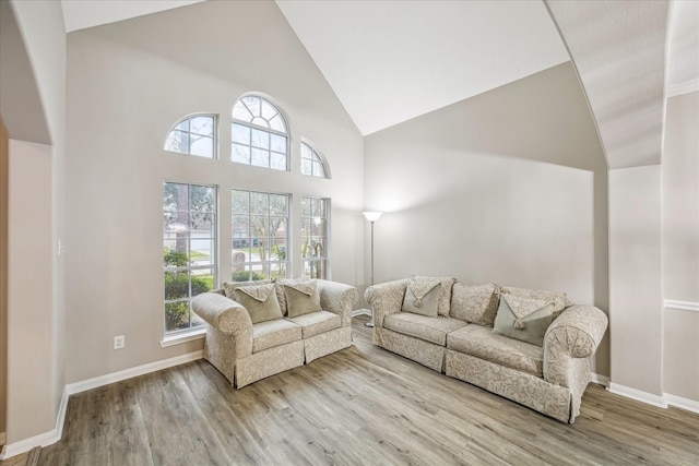 living area featuring a wealth of natural light, baseboards, high vaulted ceiling, and wood finished floors