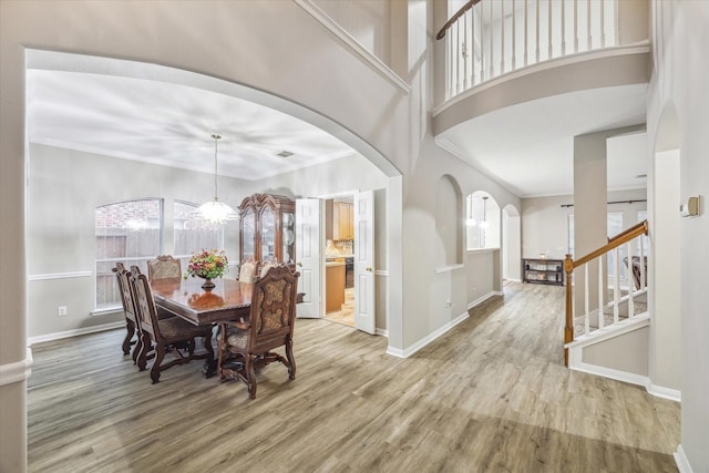 dining area featuring crown molding, light wood-style flooring, baseboards, and a towering ceiling