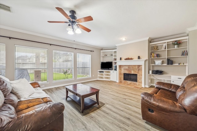 living area with visible vents, crown molding, ceiling fan, light wood-style flooring, and a tile fireplace