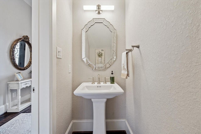 bathroom with a sink, baseboards, wood finished floors, and a textured wall