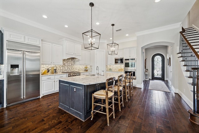 kitchen featuring visible vents, a sink, arched walkways, white cabinets, and built in appliances