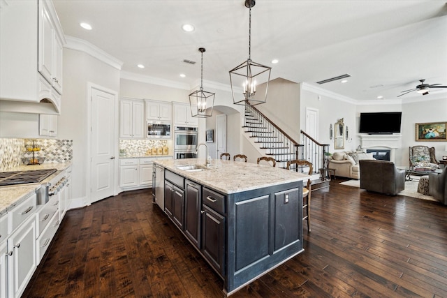 kitchen featuring a fireplace, a sink, appliances with stainless steel finishes, white cabinetry, and a kitchen breakfast bar