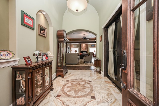 foyer entrance with baseboards, ceiling fan, arched walkways, marble finish floor, and a raised ceiling