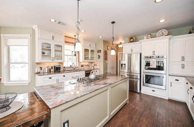 kitchen featuring a center island, glass insert cabinets, dark wood-type flooring, appliances with stainless steel finishes, and a sink