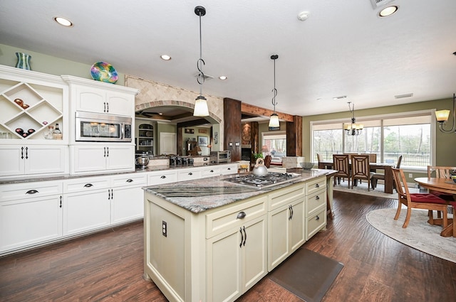 kitchen featuring a center island, dark wood finished floors, light stone counters, appliances with stainless steel finishes, and hanging light fixtures