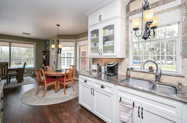 kitchen with visible vents, a sink, dark stone countertops, an inviting chandelier, and dark wood-style flooring