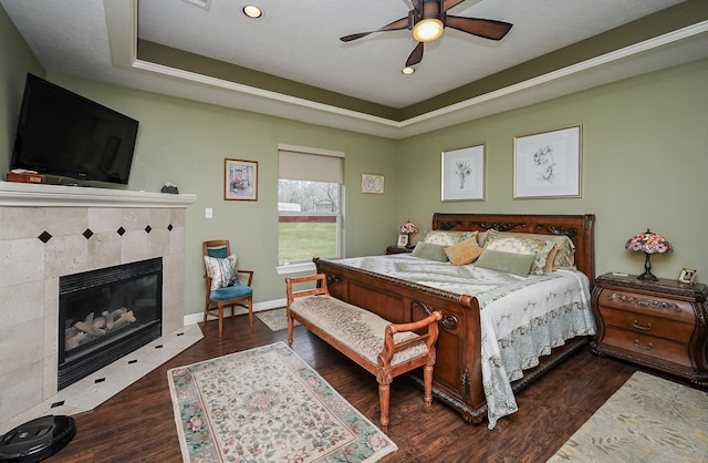 bedroom with baseboards, a tray ceiling, recessed lighting, a fireplace, and wood finished floors