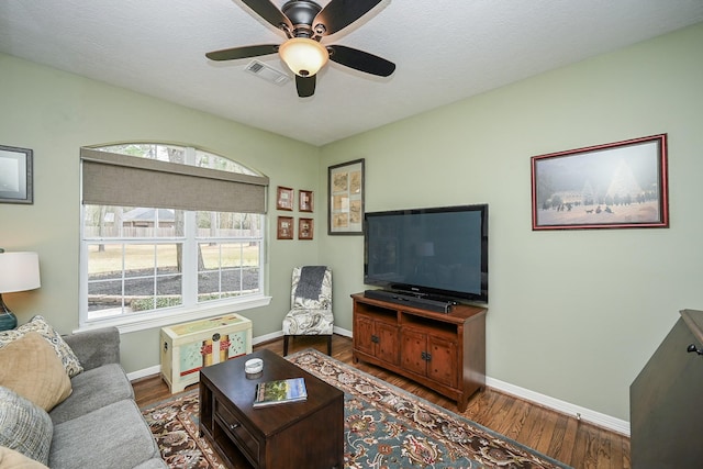 living area with a ceiling fan, wood finished floors, visible vents, and baseboards