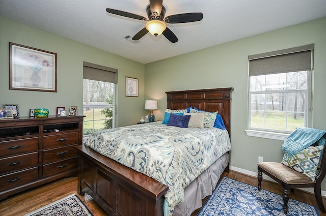 bedroom with a ceiling fan, wood finished floors, visible vents, and baseboards