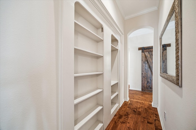 hallway featuring baseboards, dark wood finished floors, a barn door, ornamental molding, and arched walkways