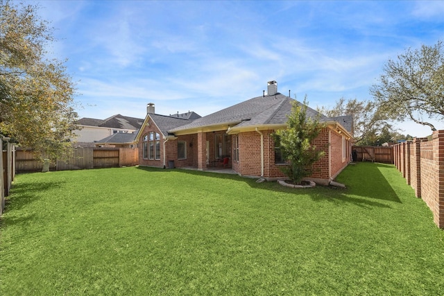 back of property featuring brick siding, a lawn, a fenced backyard, and roof with shingles